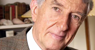 Festival di Spoleto founder sits contemplatively near bookshelf in portrait