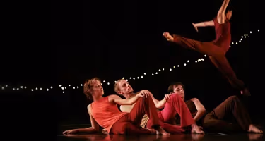 Danzatori in rosso sul palco al Festival di Spoleto, illuminati da luci soffuse