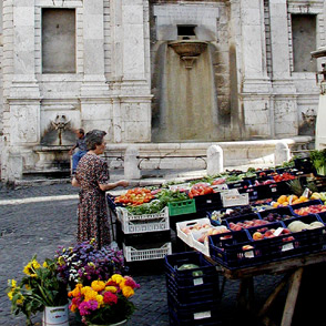 Colorful produce stand at Spoleto Festival di market near historic stone fountain