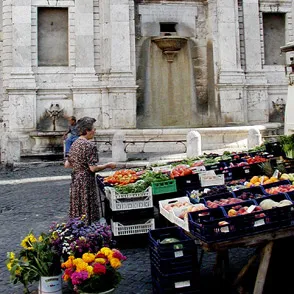 Colorful produce stand at Spoleto Festival di market near historic stone fountain