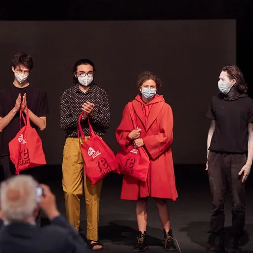 Quattro performer con maschere al Festival di Spoleto, borse rosse in mano