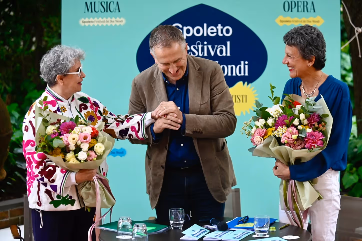 Tre persone sorridenti al Festival di Spoleto con bouquet colorati