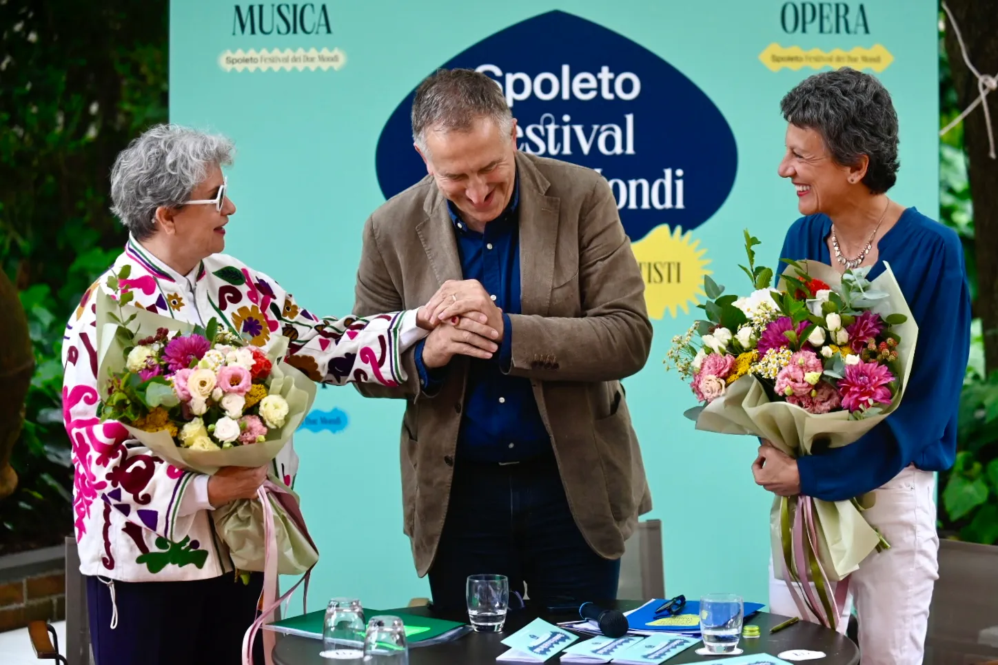 Three people with flower bouquets at Spoleto Festival di Spoleto press conference