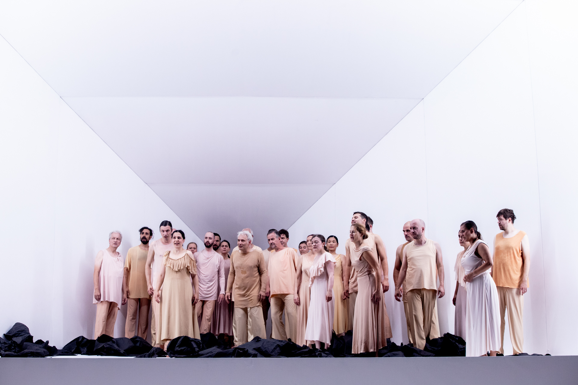 Performers in beige costumi al Festival di Spoleto, schierati su palcoscenico minimale