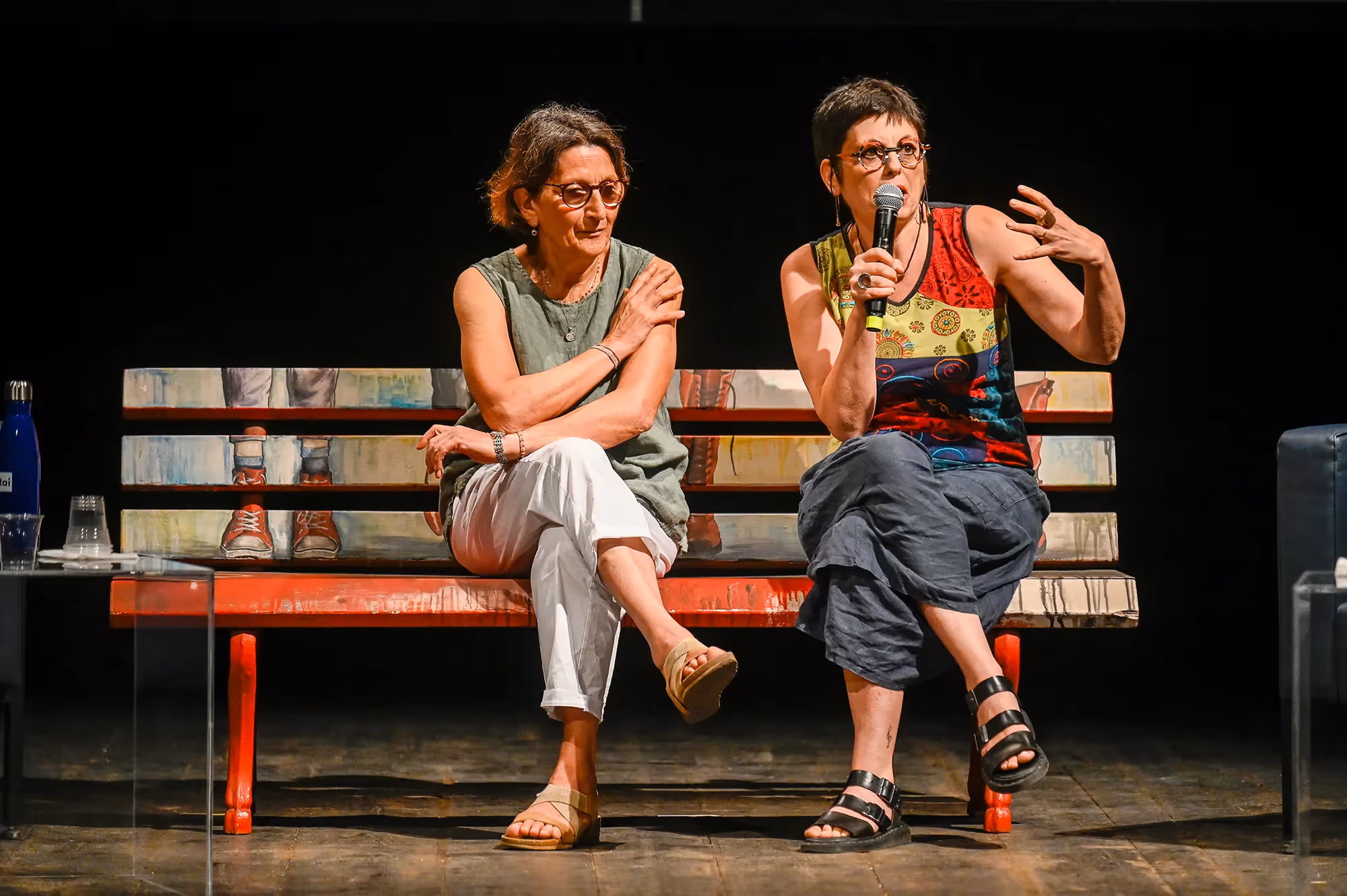 Due donne al Festival di Spoleto, sedute su una panca rossa, conversano