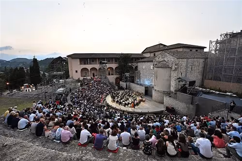 Crowded outdoor concert at Festival di Spoleto with orchestra and historic buildings