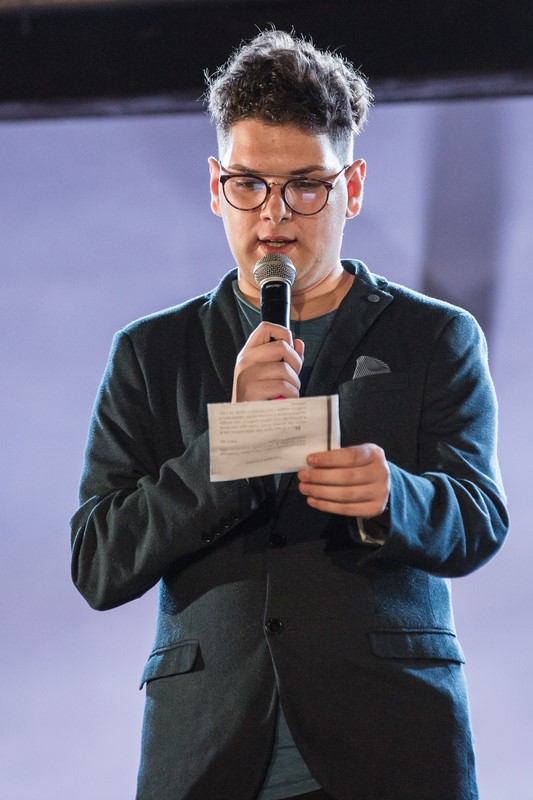 Speaker presenting at Festival di Spoleto event, wearing glasses and black jacket