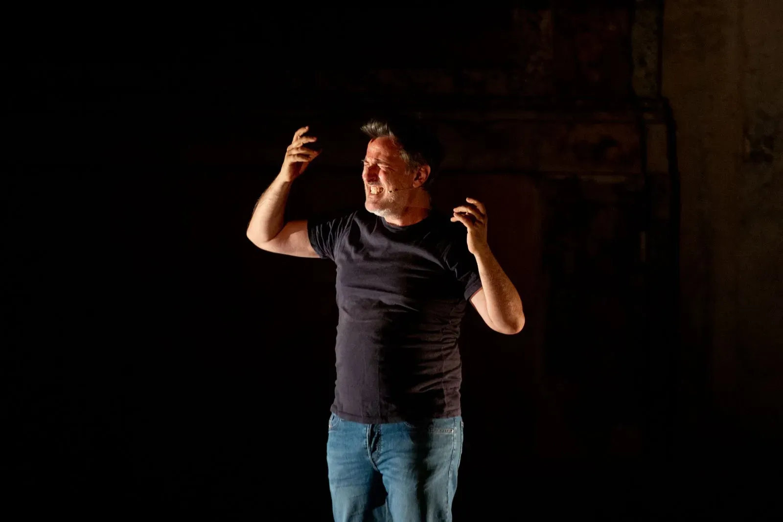 Performer drammatico sul palco al Festival di Spoleto, gesti intensi nell'oscurità
