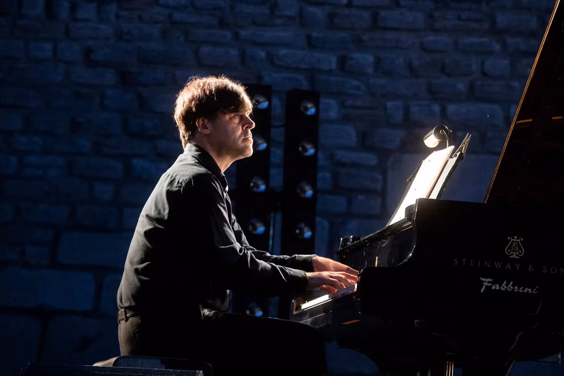 Pianist performing at Festival di Spoleto, illuminated against stone wall backdrop