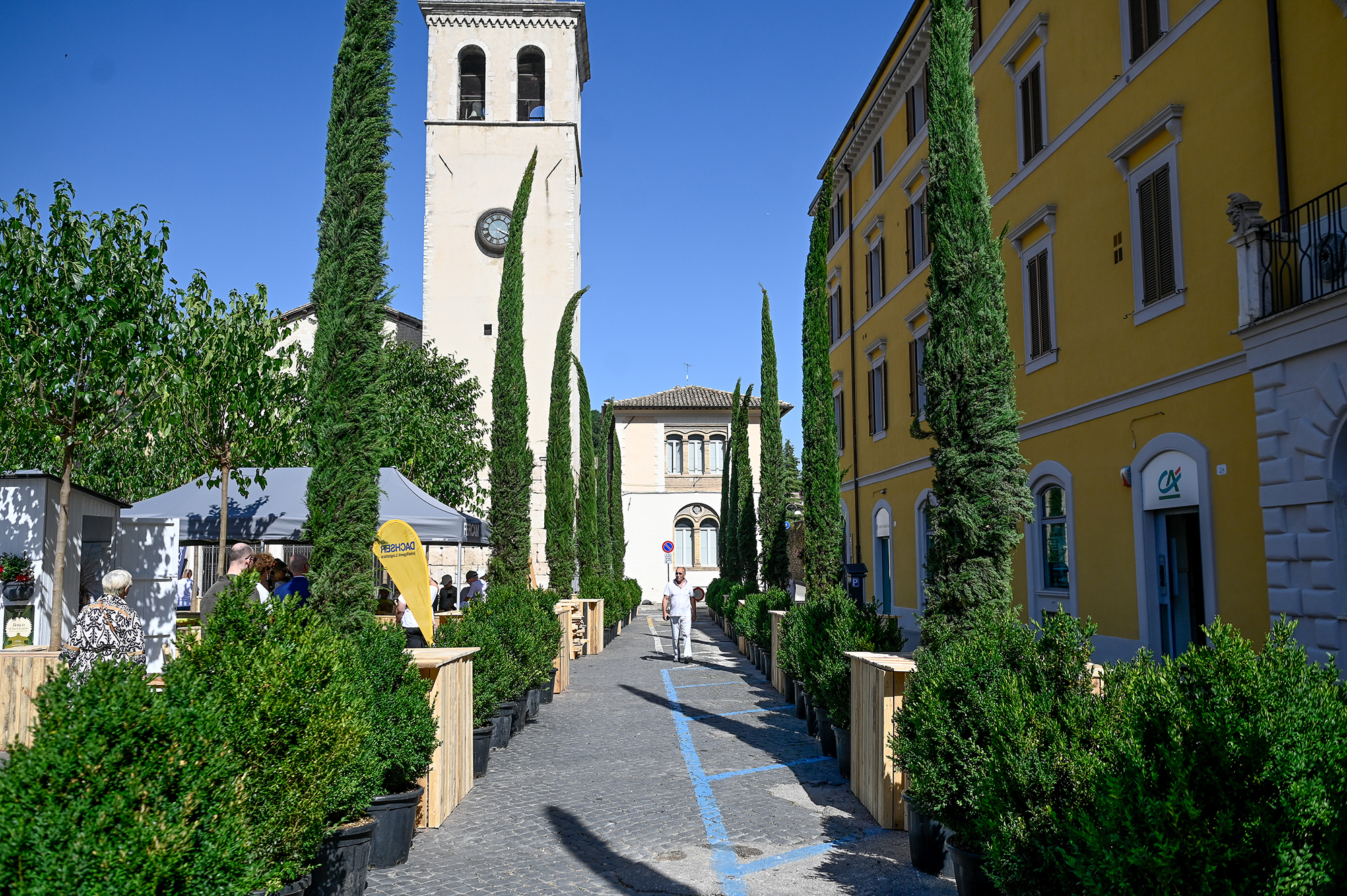 Veduta del Festival di Spoleto con torre campanaria e cipressi in una giornata soleggiata