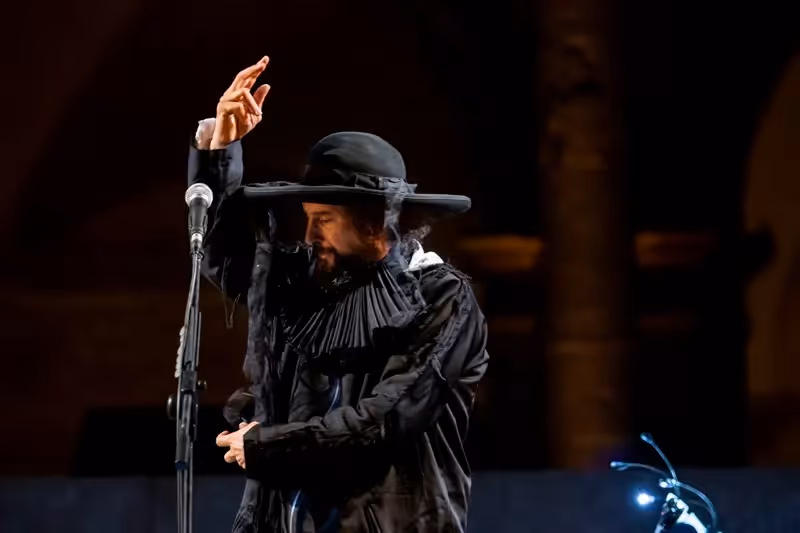 Artista in costume nero si esibisce al Festival di Spoleto, gesto drammatico