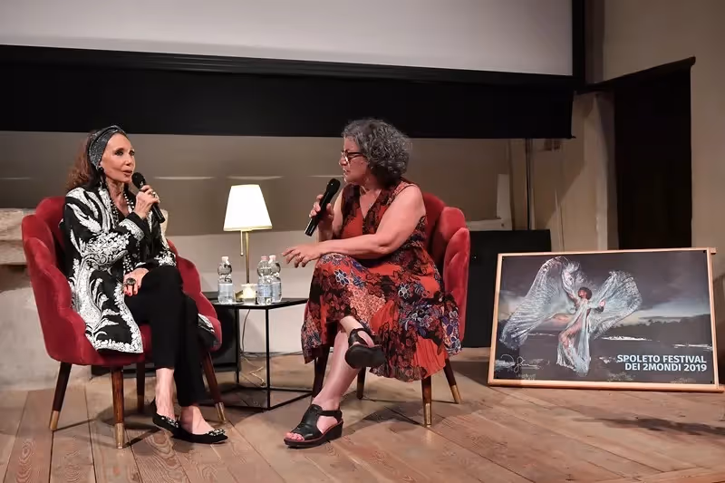 Two women speak at Festival di Spoleto event with artistic poster displayed