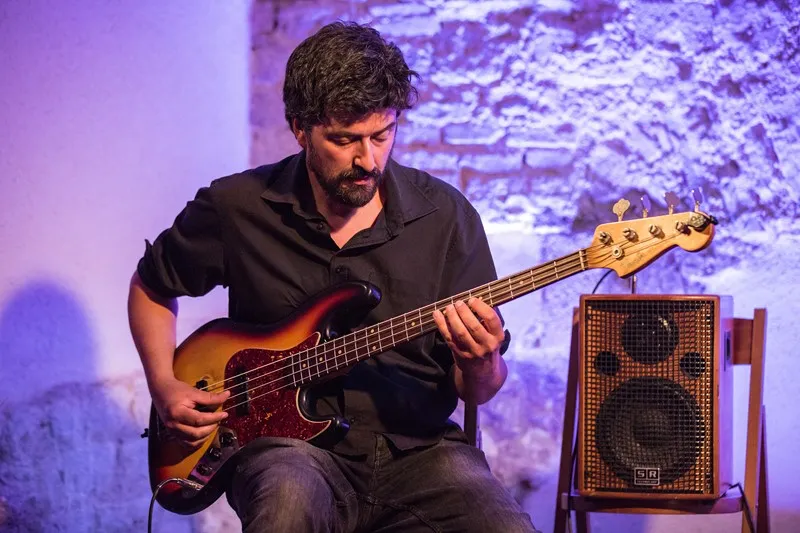 Bass guitarist performs at Festival di Spoleto with purple stone wall backdrop