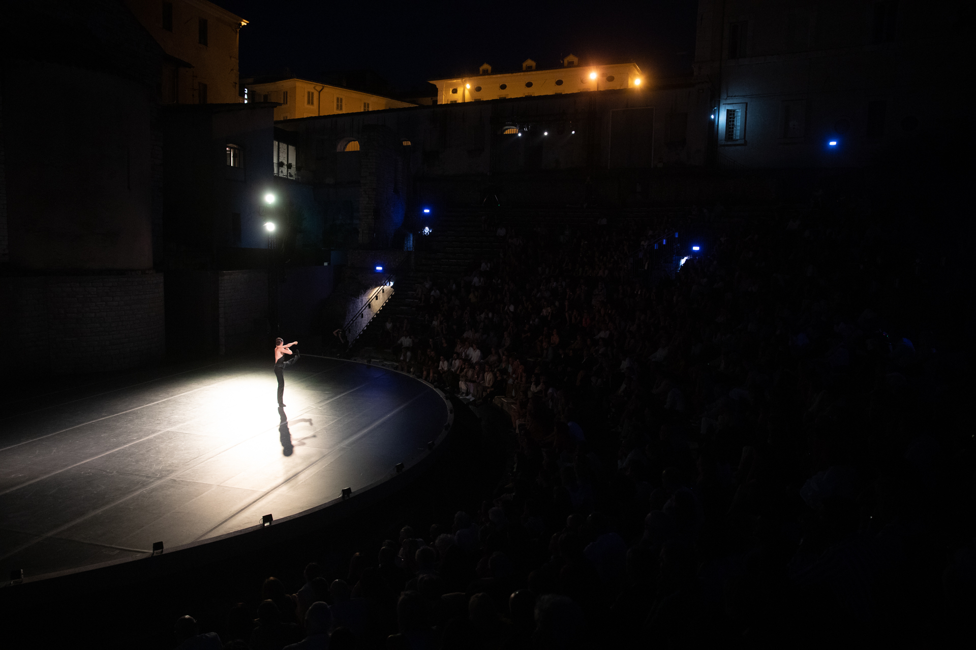 Performer solitario illuminato sul palco durante il Festival di Spoleto