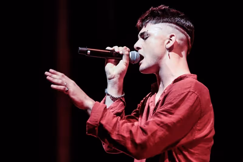 Singer performing at Festival di Spoleto, wearing red shirt, singing passionately