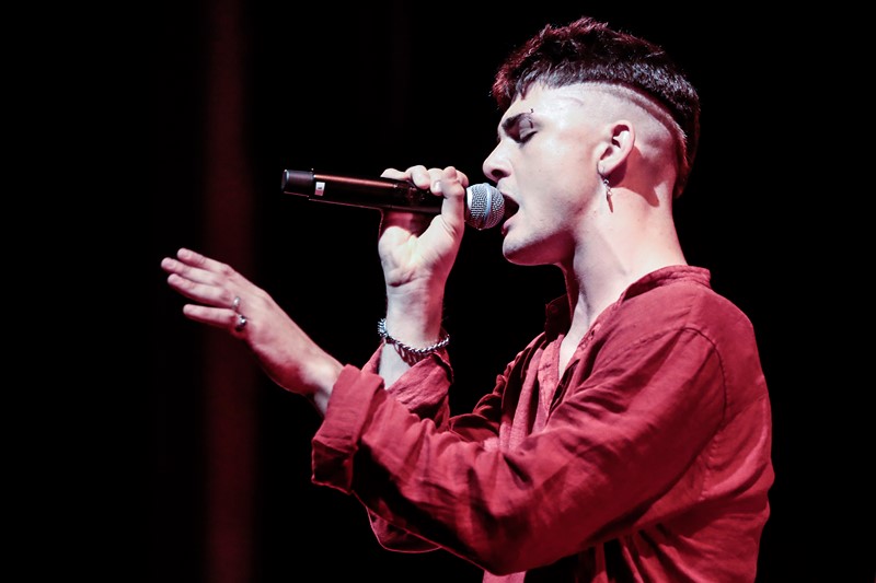 Singer performing at Festival di Spoleto, wearing red shirt, singing passionately