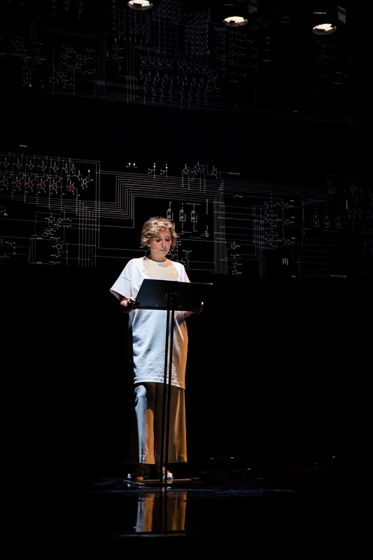 Performer reading at Festival di Spoleto against intricate technical backdrop