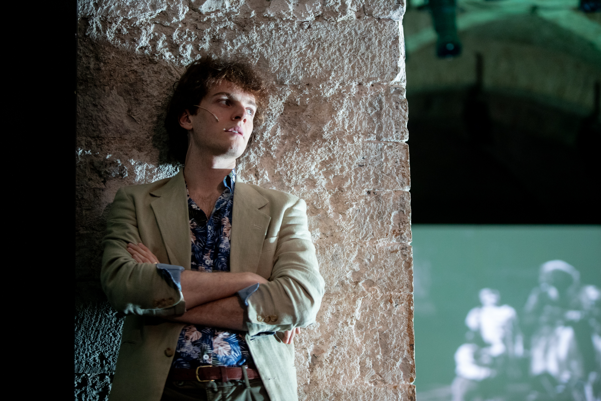 Festival di Spoleto performer leans against stone wall in stylish outfit