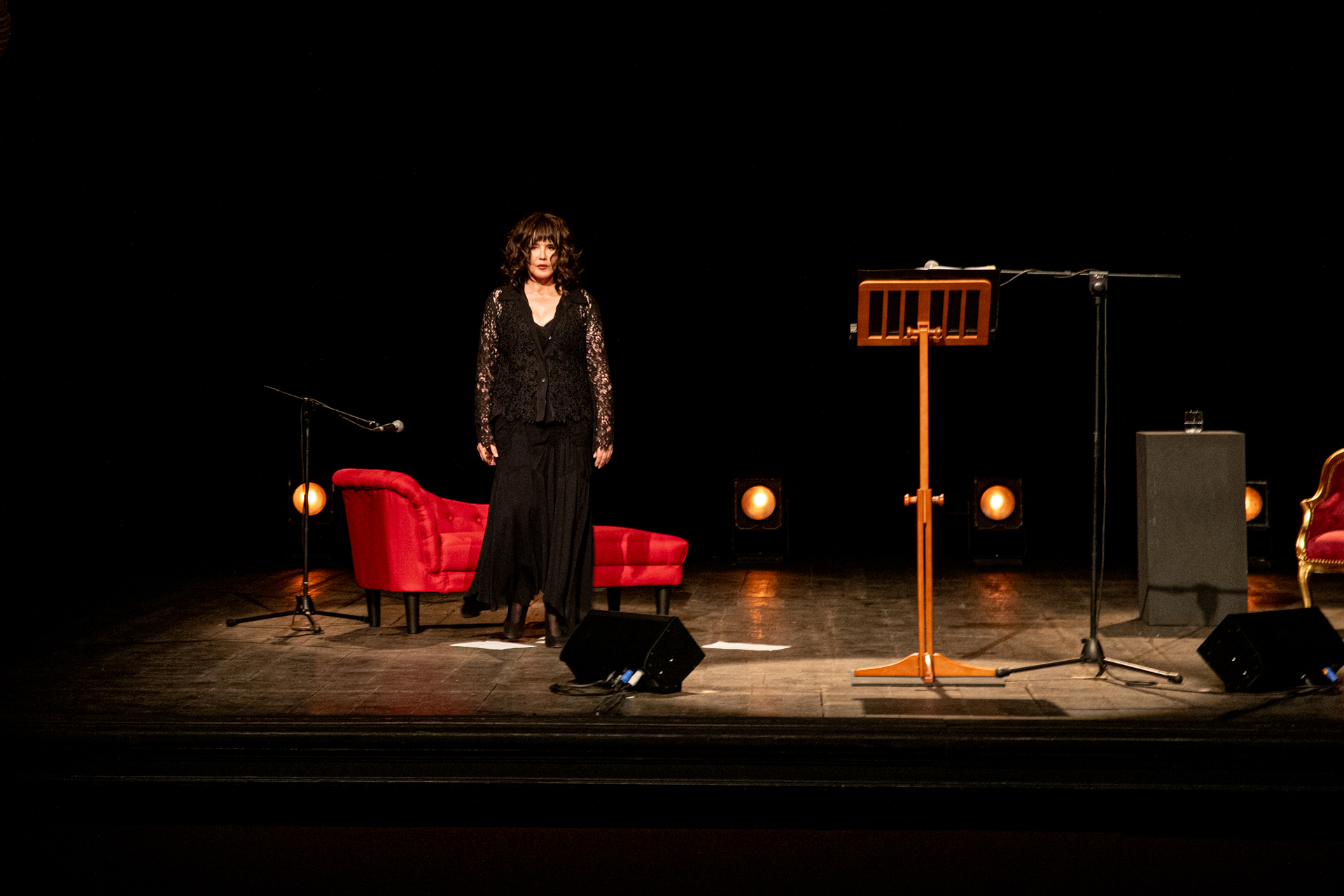 Performer on stage at Festival di Spoleto, wearing black, with red chairs