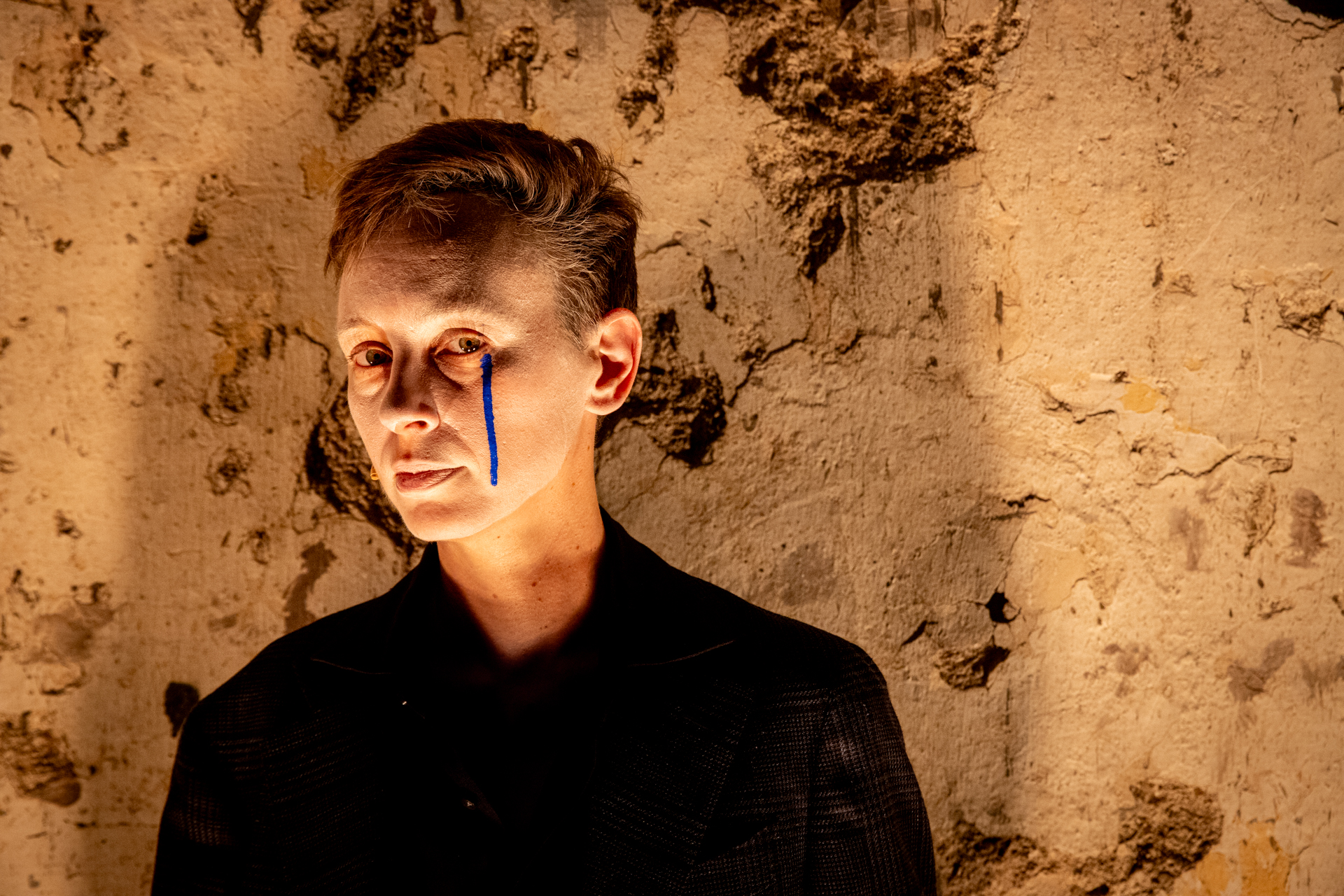 Artista al Festival di Spoleto con linea blu sul viso, sfondo texture