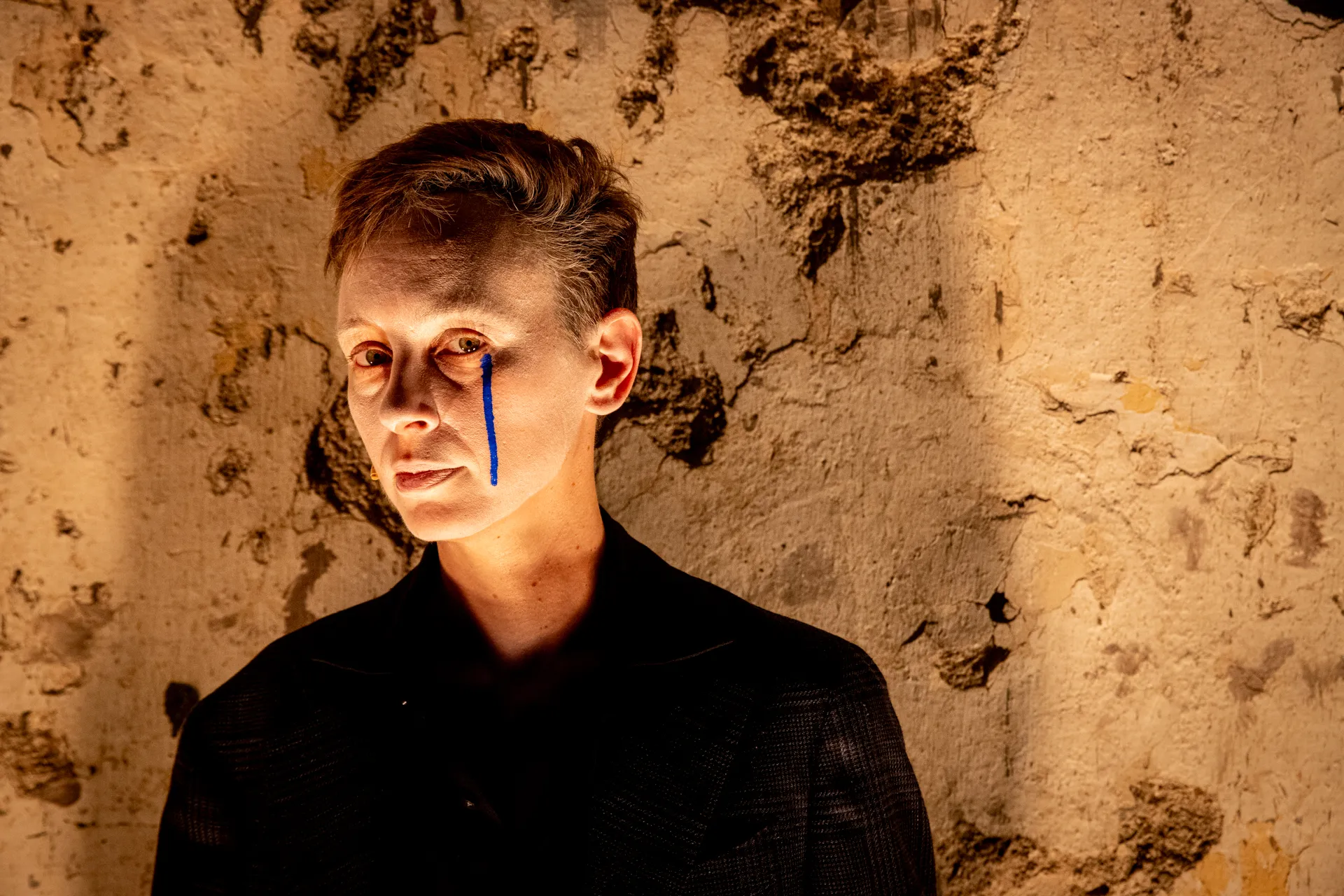 Artista al Festival di Spoleto con linea blu sul viso, sfondo texture