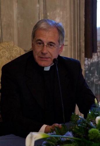 Clergyman at Festival di Spoleto event, seated with floral arrangement nearby