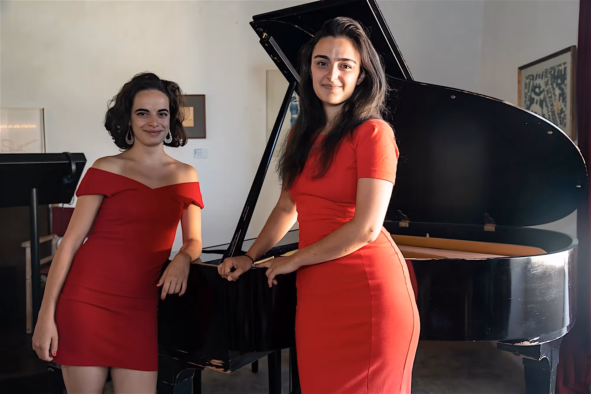 Two musicians in red dresses at Festival di Spoleto, posing with grand piano