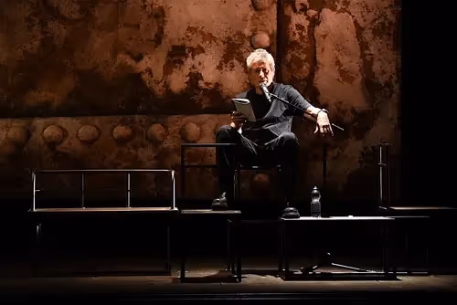 Elder performer on stage at Festival di Spoleto, sitting alone in dramatic lighting
