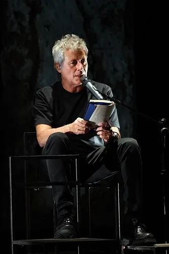 Author reading at Festival di Spoleto, seated on stage with book and microphone