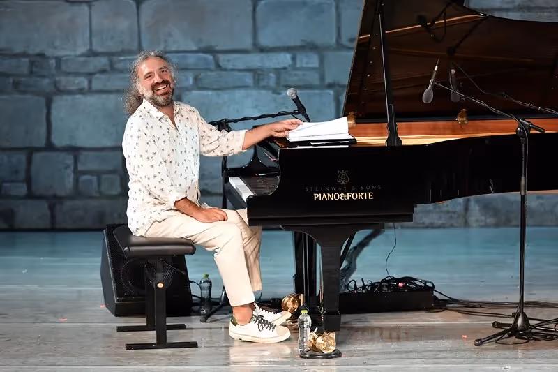 Pianist performing at Festival di Spoleto, smiling by grand piano on stone stage