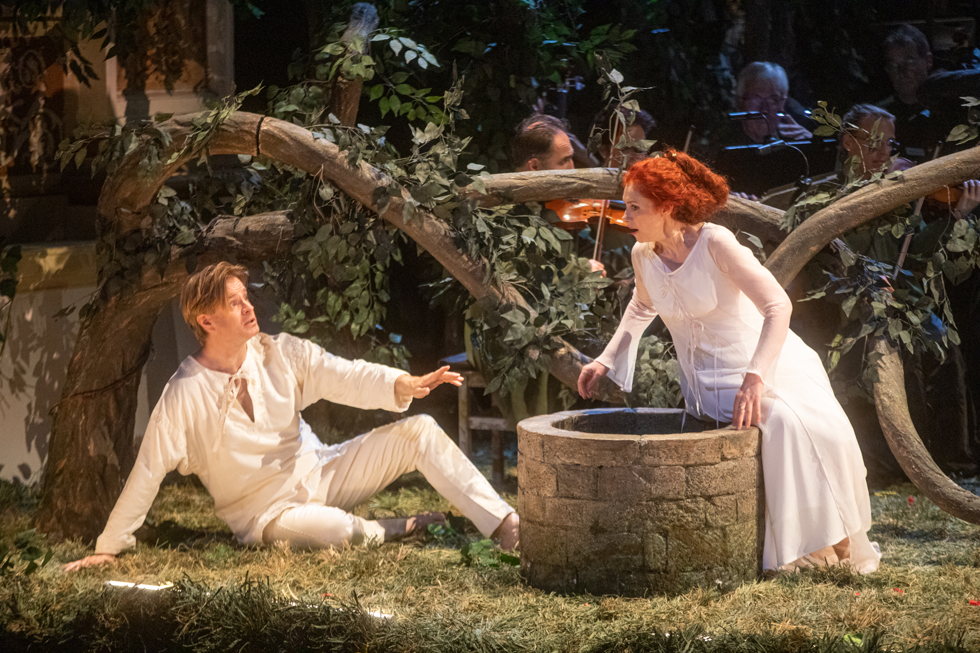 Scena teatrale al Festival di Spoleto, attori in bianco accanto a un pozzo