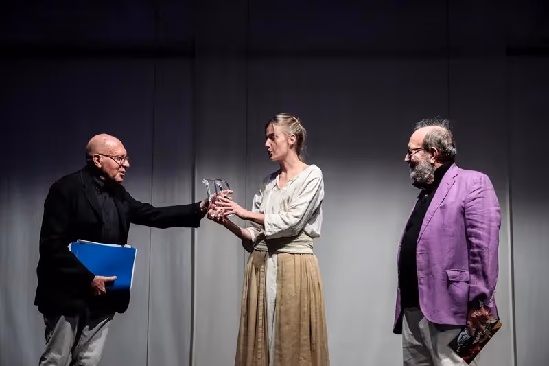 Scena teatrale al Festival di Spoleto con tre attori su sfondo grigio
