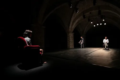 Scena drammatica al Festival di Spoleto con attori su palcoscenico buio