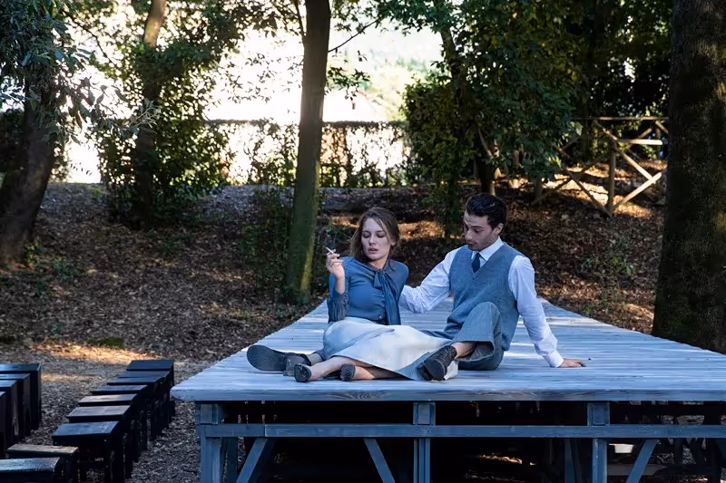 Two performers relaxing at Festival di Spoleto, seated on wooden stage outdoors