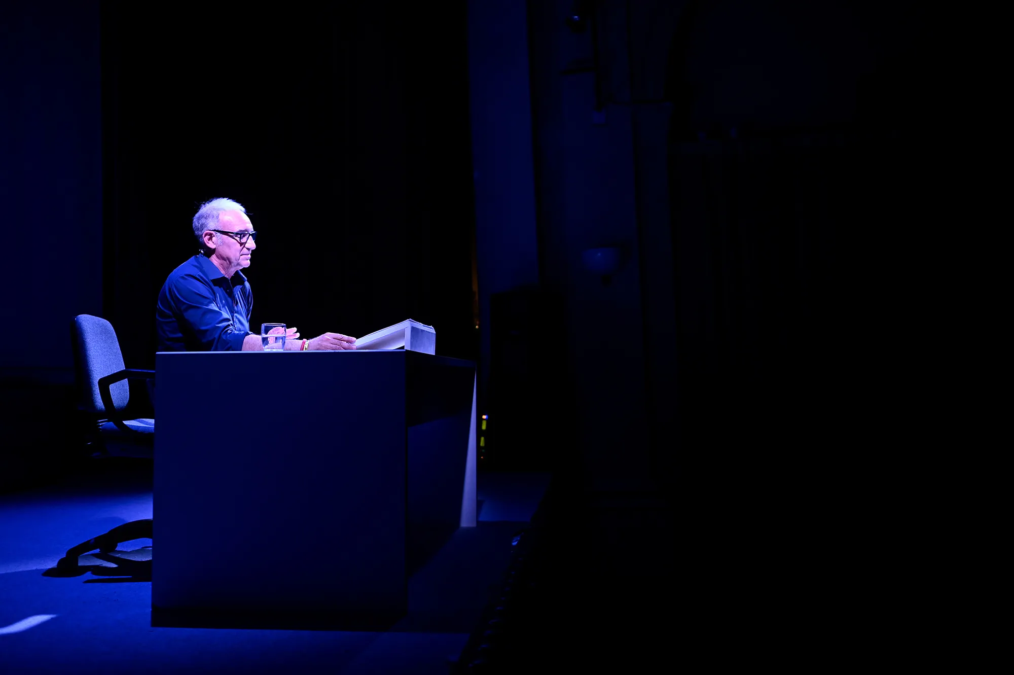 Anziano relatore sul palco durante il Festival di Spoleto, illuminato dal blu