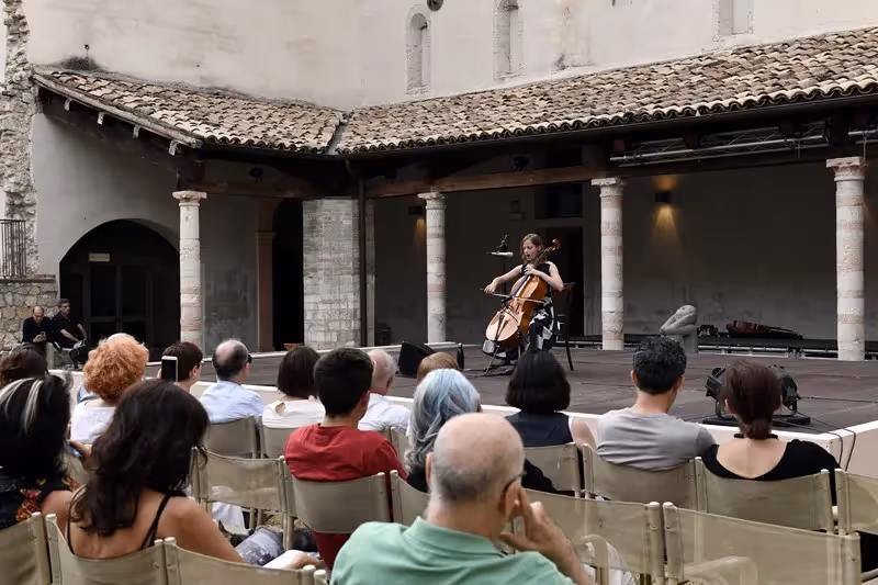 Cellist performing at Festival di Spoleto in historic stone courtyard with attentive audience