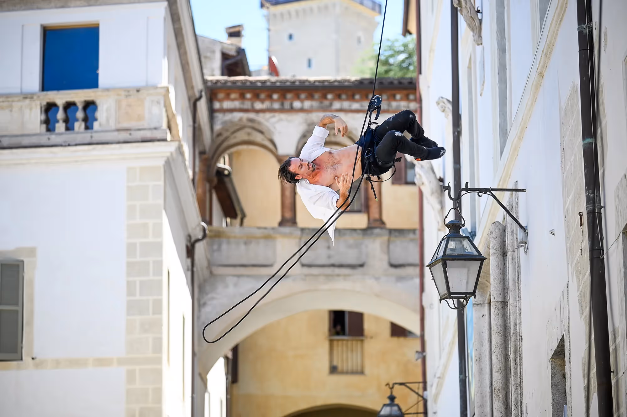 Performer suspended on wire at Festival di Spoleto, dramatic urban backdrop