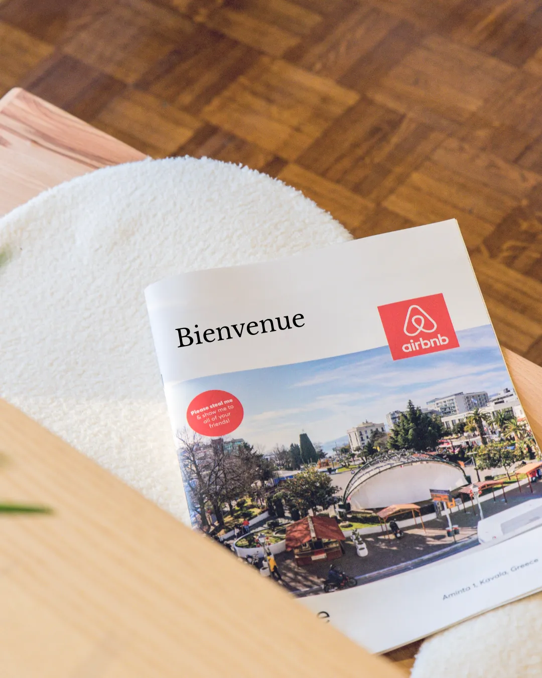 Magazine with Airbnb logo and 'Bienvenue' text on a round white textured surface next to wooden furniture.