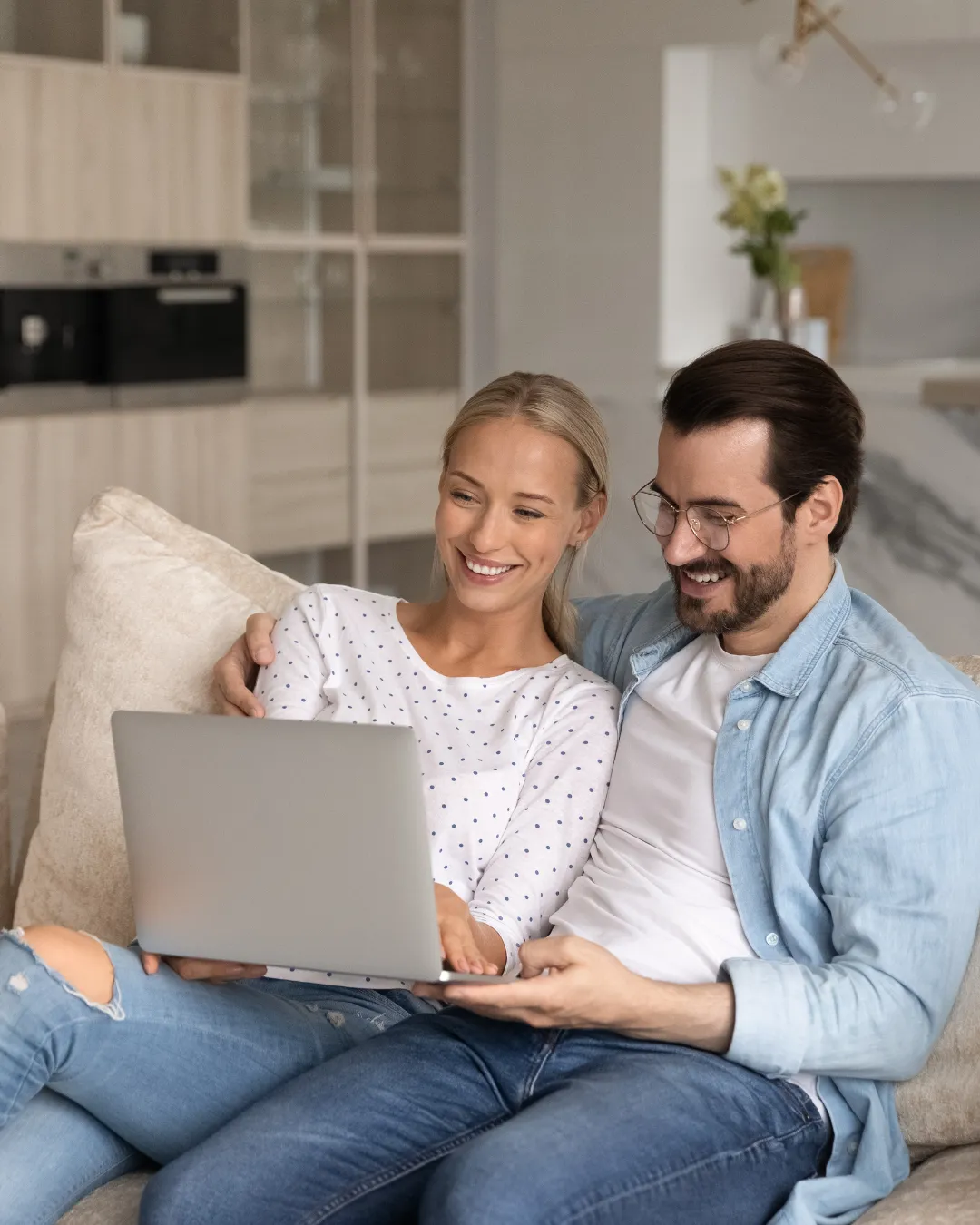Smiling couple sitting on a couch looking at a laptop together in a modern living room.