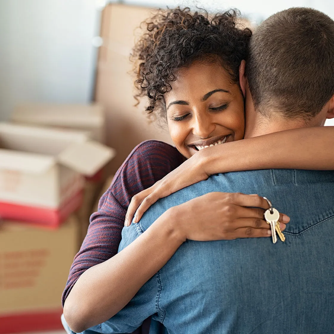 woman hugging partner while holding keys to their new home