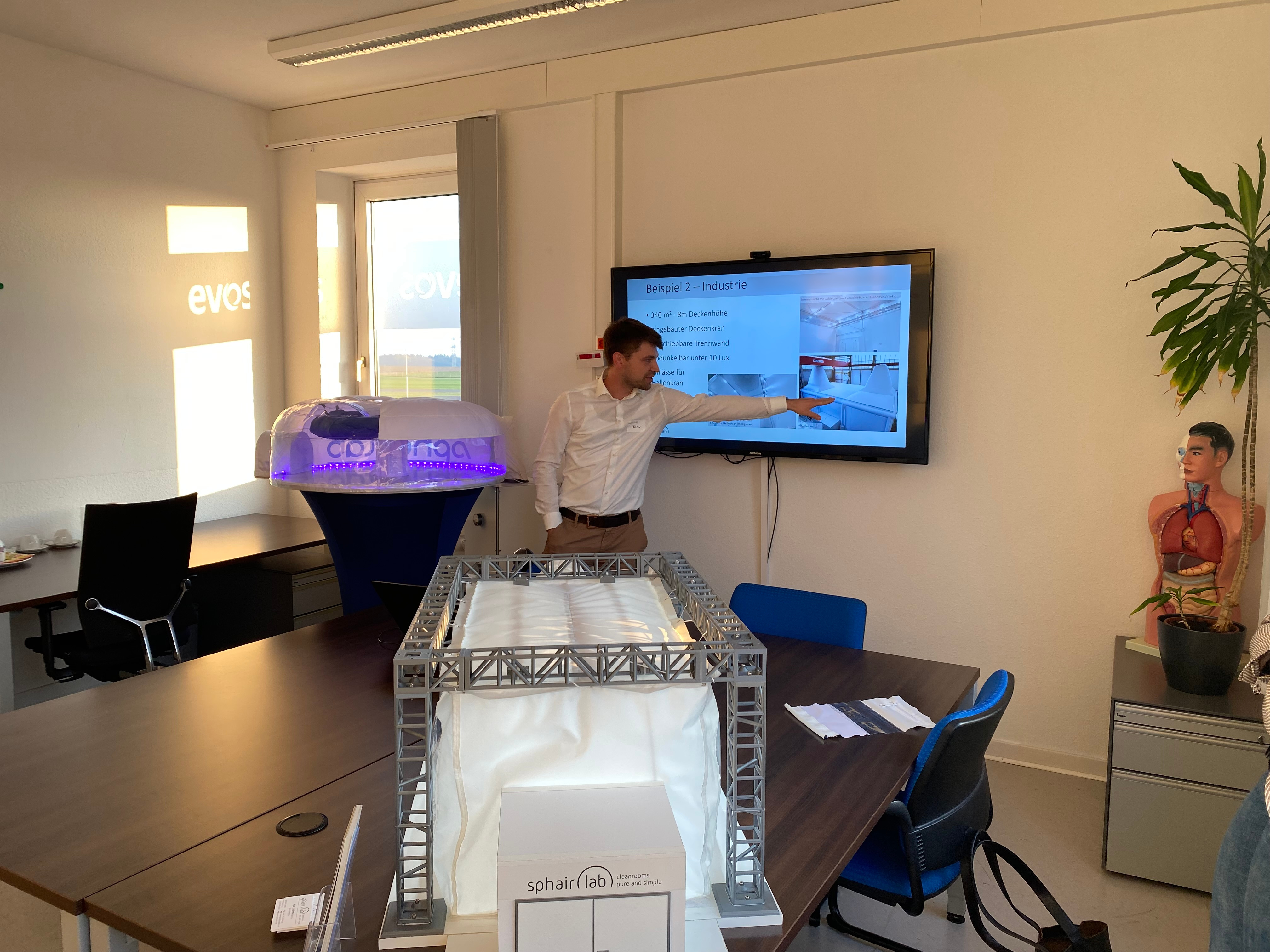 Two miniature cleanrooms. In the background Max Lindemann is showing something on a presentation slide.