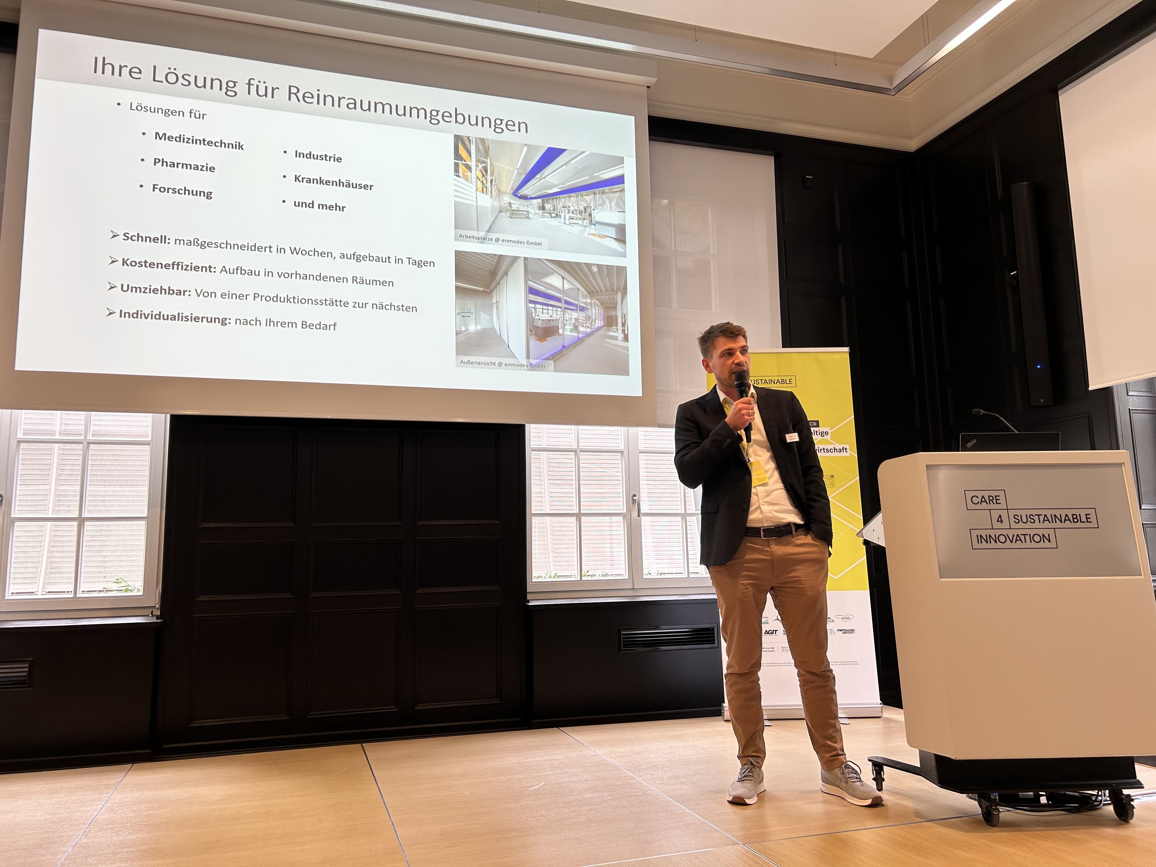 Dr. Max Lindemann stands on stage during the startup pitches. Behind him is a slide highlighting sphairlab’s USPs (fast, cost-effective, mobile, customized)