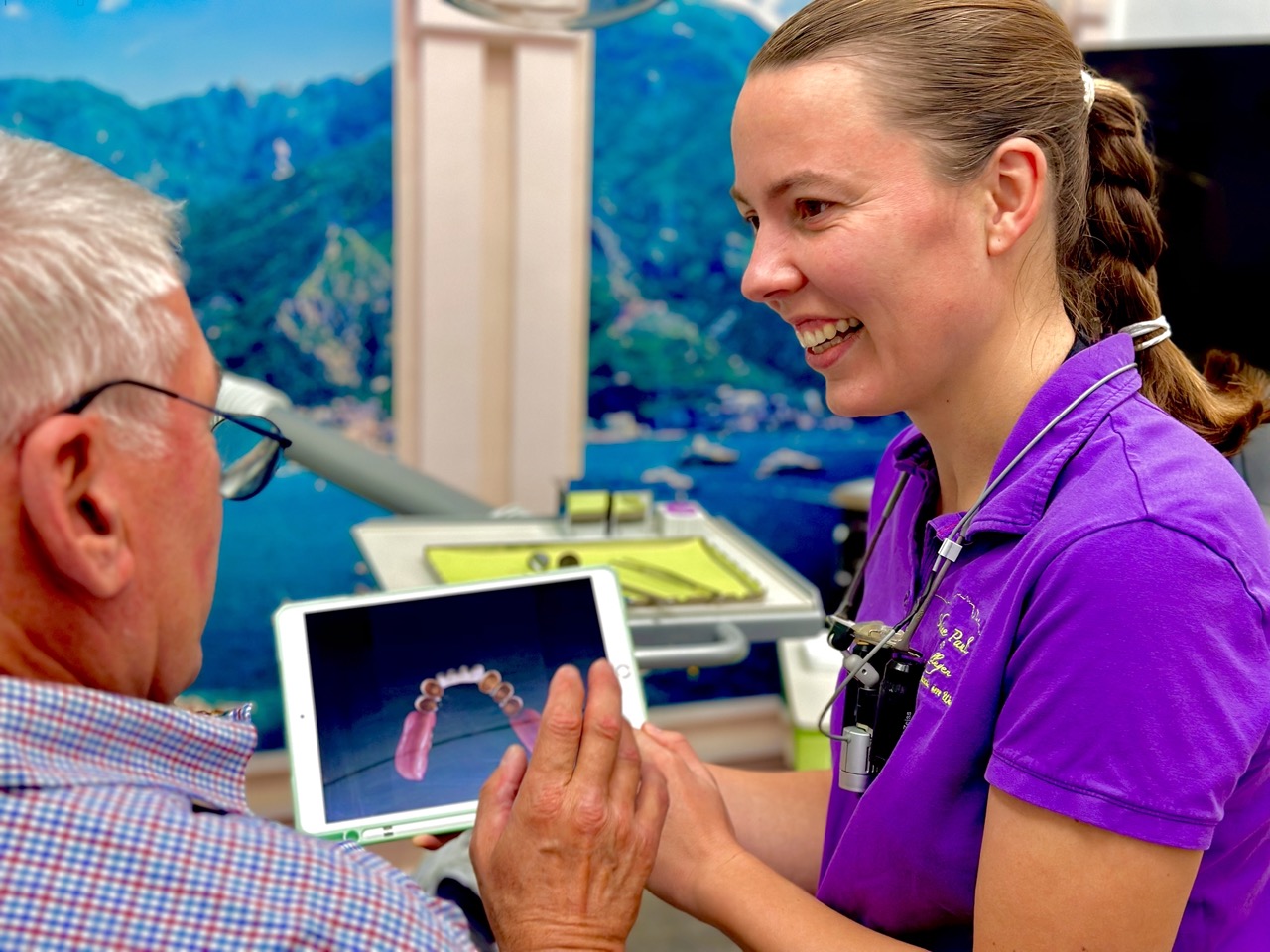 Zahnärztin zeigt einem älteren Patienten ein 3D-Modell des Gebisses auf einem Tablet und bespricht die Behandlung.