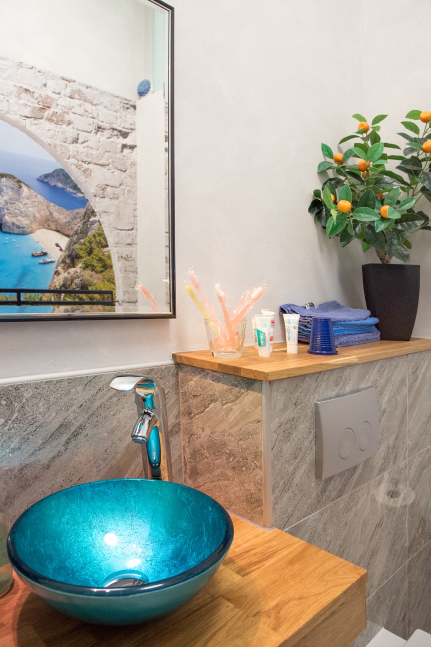 Modernes Waschbecken mit türkisfarbener Glasschale, dekorativer Pflanze und Pflegeartikeln in einem stilvollen Praxisbad.