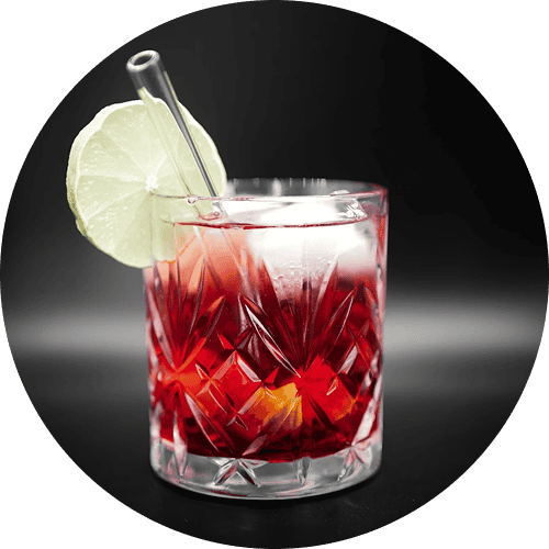 Glass of red cocktail with ice cubes, a lime slice garnish, and a clear straw in a textured glass.