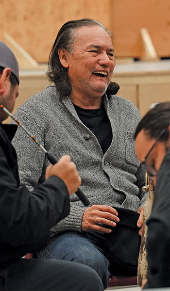 A man sits in a drum circle laughing with others.
