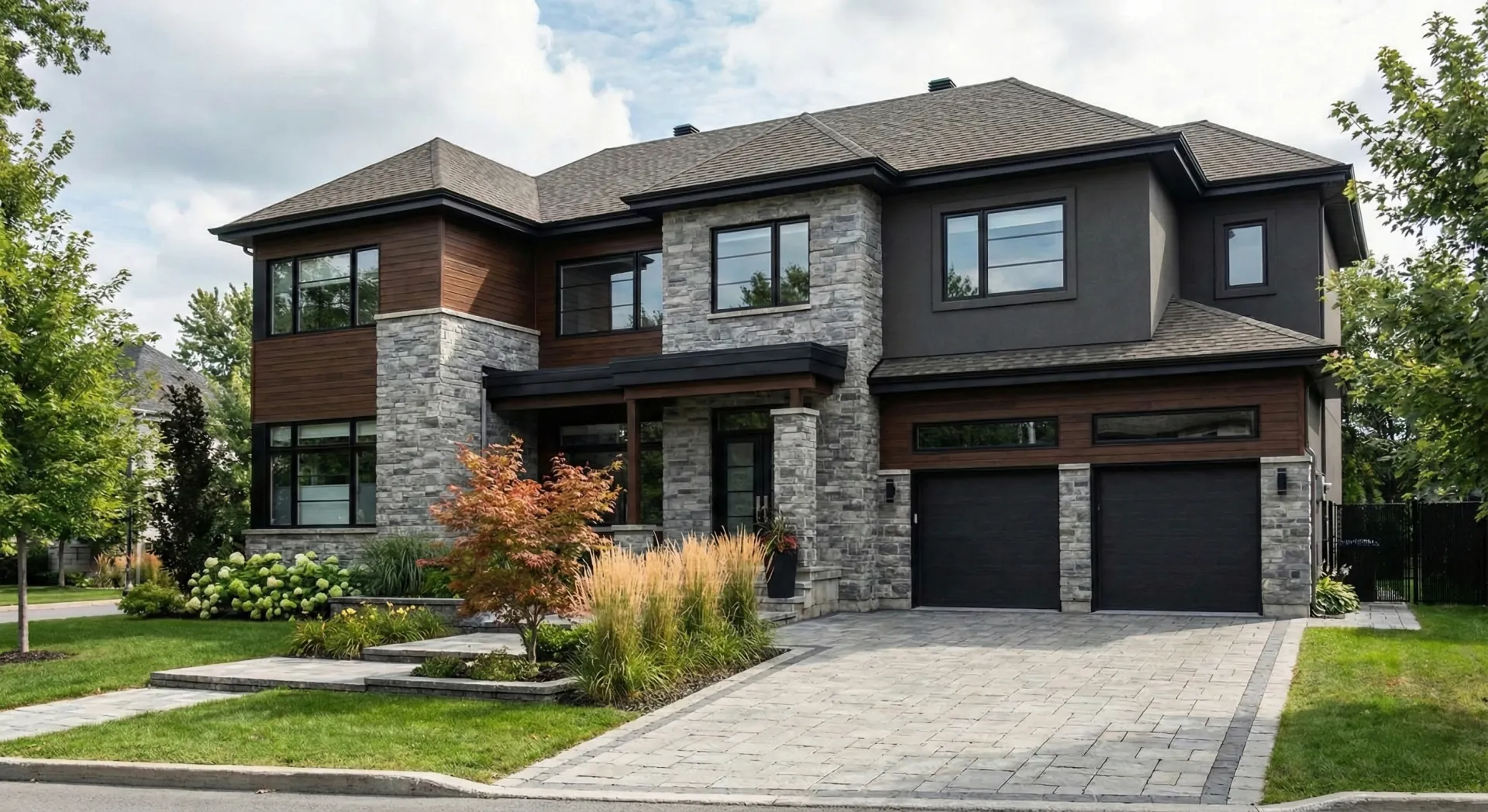 Maison contemporaine à deux étages avec revêtement en pierre grise, bois naturel et stucco foncé, garage double et aménagement paysager soigné