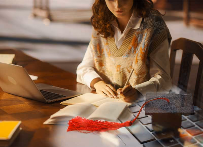 Student studying with laptop, books, and graduation cap with red tassel