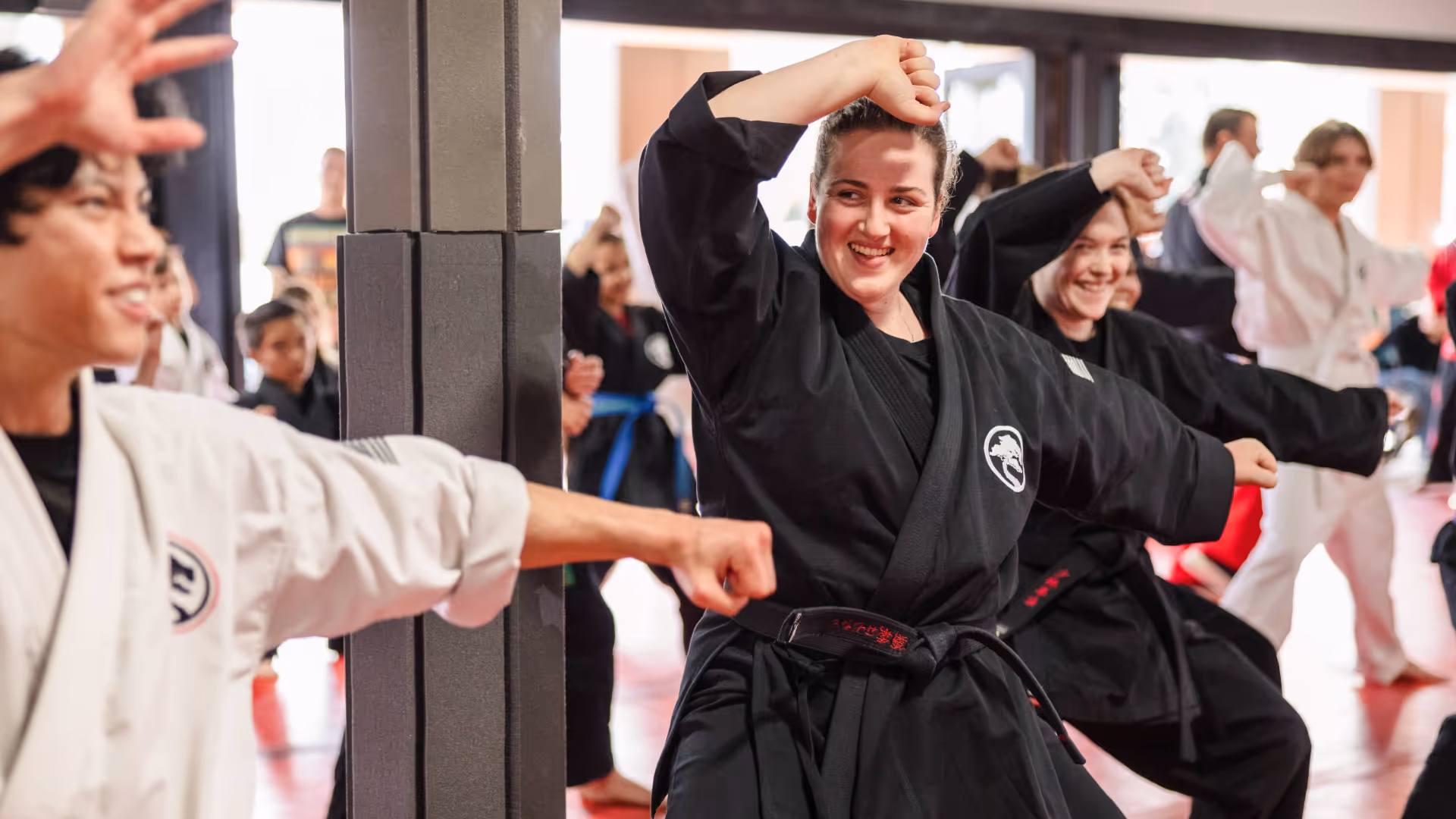 A group of adult karate students are smiling together as they practice forms during karate class.