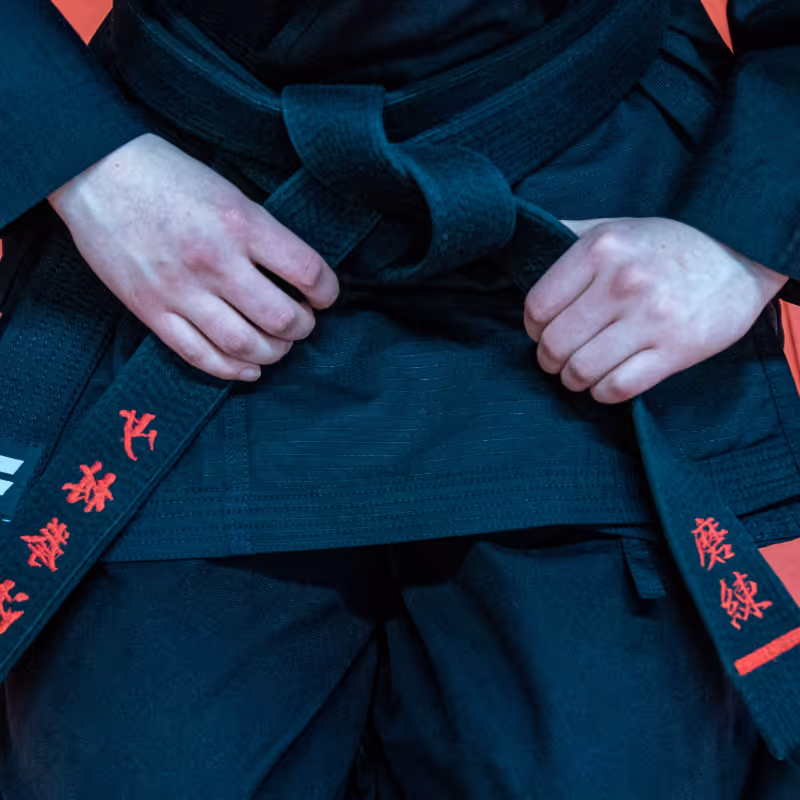 A person wearing a karate gi is tightening their green karate belt around their waist.